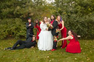 Wedding party strikes fun poses on autumn lawn wearing red and white attire.