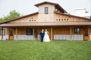 Newlyweds pose in front of rustic wooden barn venue with green lawn.