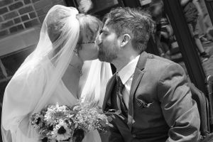 A romantic black and white wedding kiss between newlyweds with the bride holding a floral bouquet.