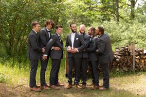 Groomsmen gather in casual moment wearing dark suits in outdoor woodland setting.