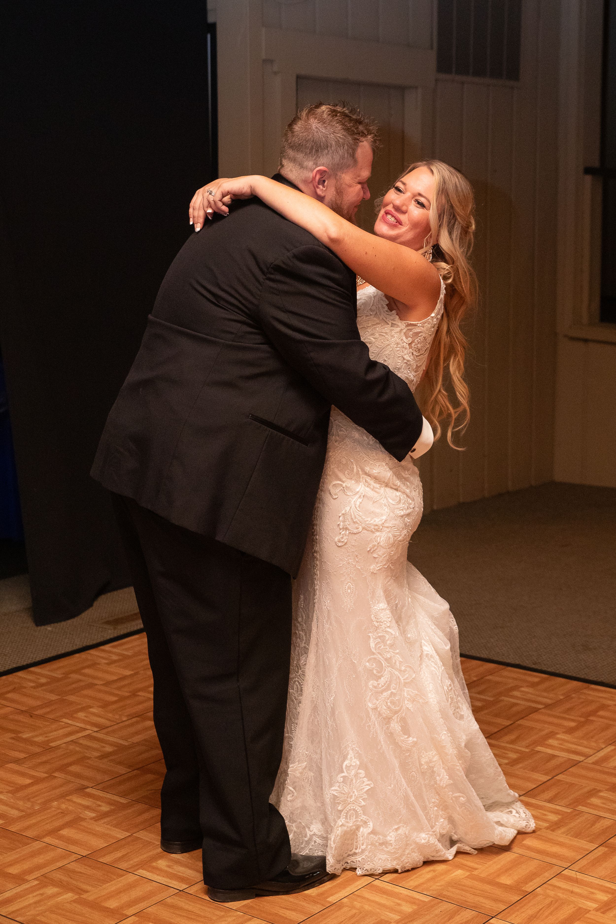 A couple shares their first dance in formal wedding attire on a wooden dance floor.