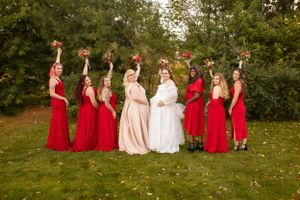 Bridal party in red dresses celebrates outdoors with joyful poses on green lawn.