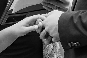 Black and white close-up of hands exchanging wedding rings during ceremony.