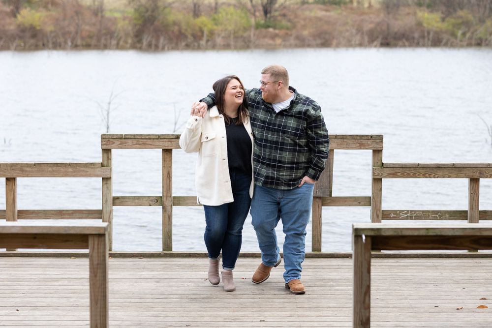 Two people walking and laughing together on wooden pier over calm water.