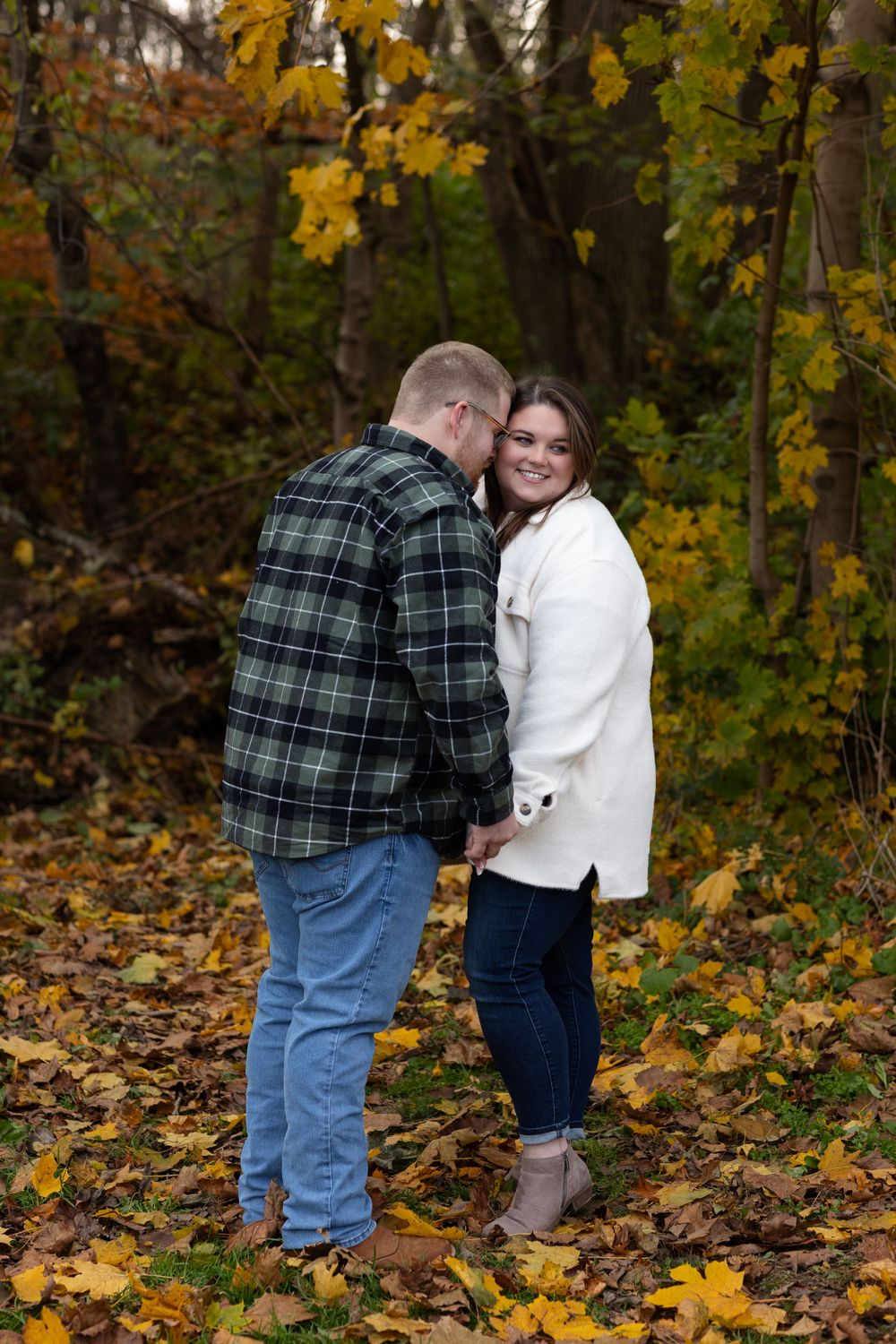 Couple sharing intimate moment among fall foliage in wooded setting.