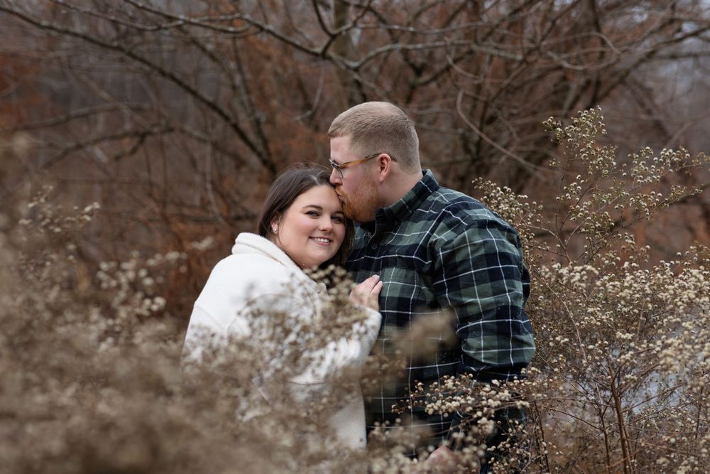 Couple embracing in natural setting with dried flowers in foreground.