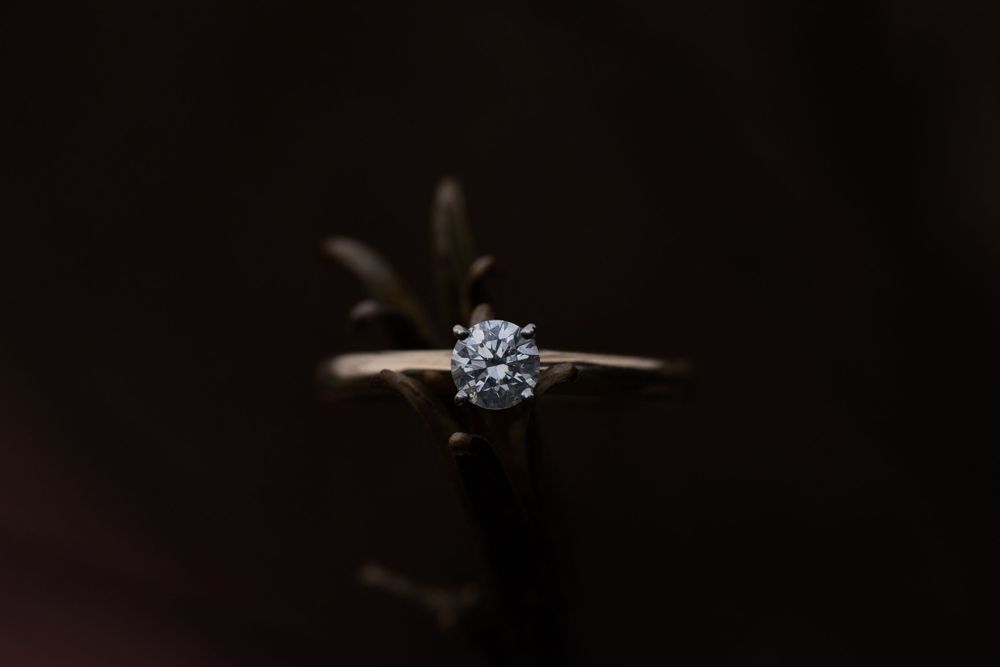 Close-up of a solitaire diamond ring on a delicate gold band against a dark background.