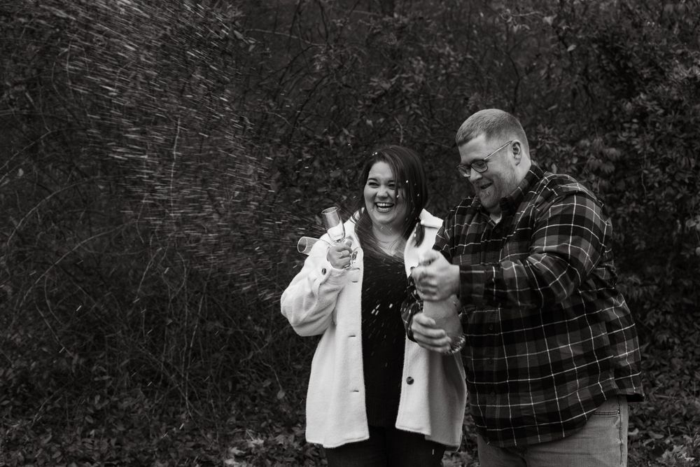 Black and white photo of a couple celebrating with champagne bottles outdoors.