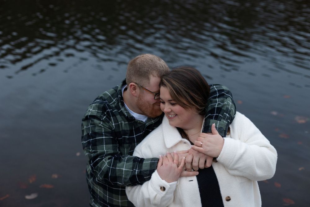 A tender moment shared between a couple against a peaceful lakeside backdrop.