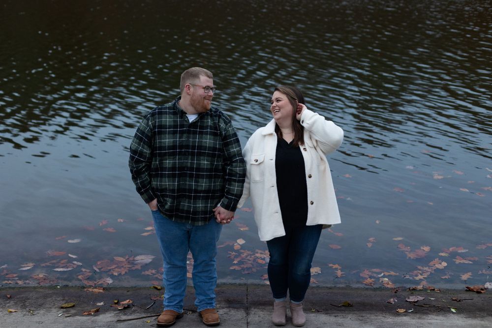 A couple shares a lighthearted moment while walking along a waterfront path in autumn.