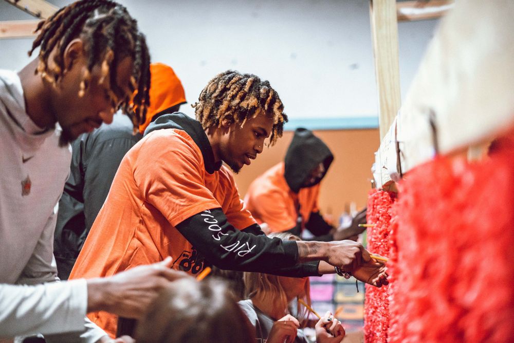 Athletes gathered around table at sports event wearing orange team apparel.