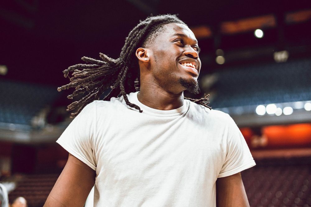 Basketball player in white t-shirt smiling in indoor arena setting.