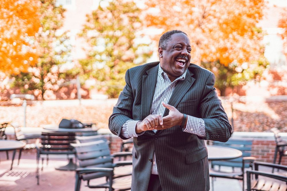 Person in suit jacket gesturing outdoors during autumn season.