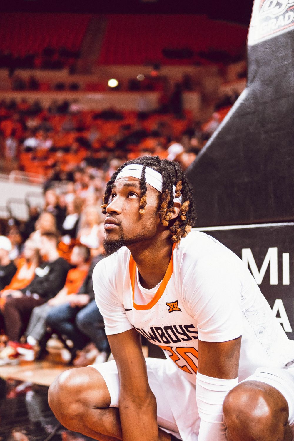 Basketball player in white Cowboys uniform sits courtside during game.