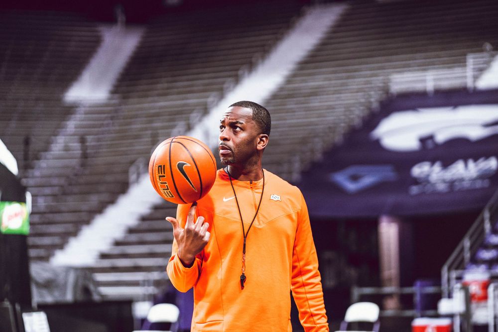 Basketball player in orange sweatshirt practices ball handling drills in empty stadium.