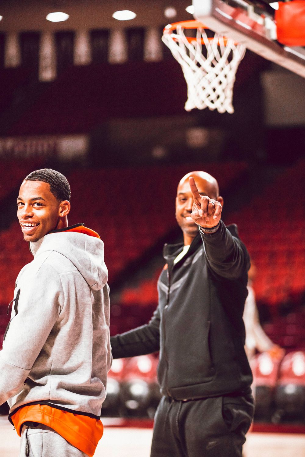 Basketball players and coach interact during practice session near a basketball hoop.
