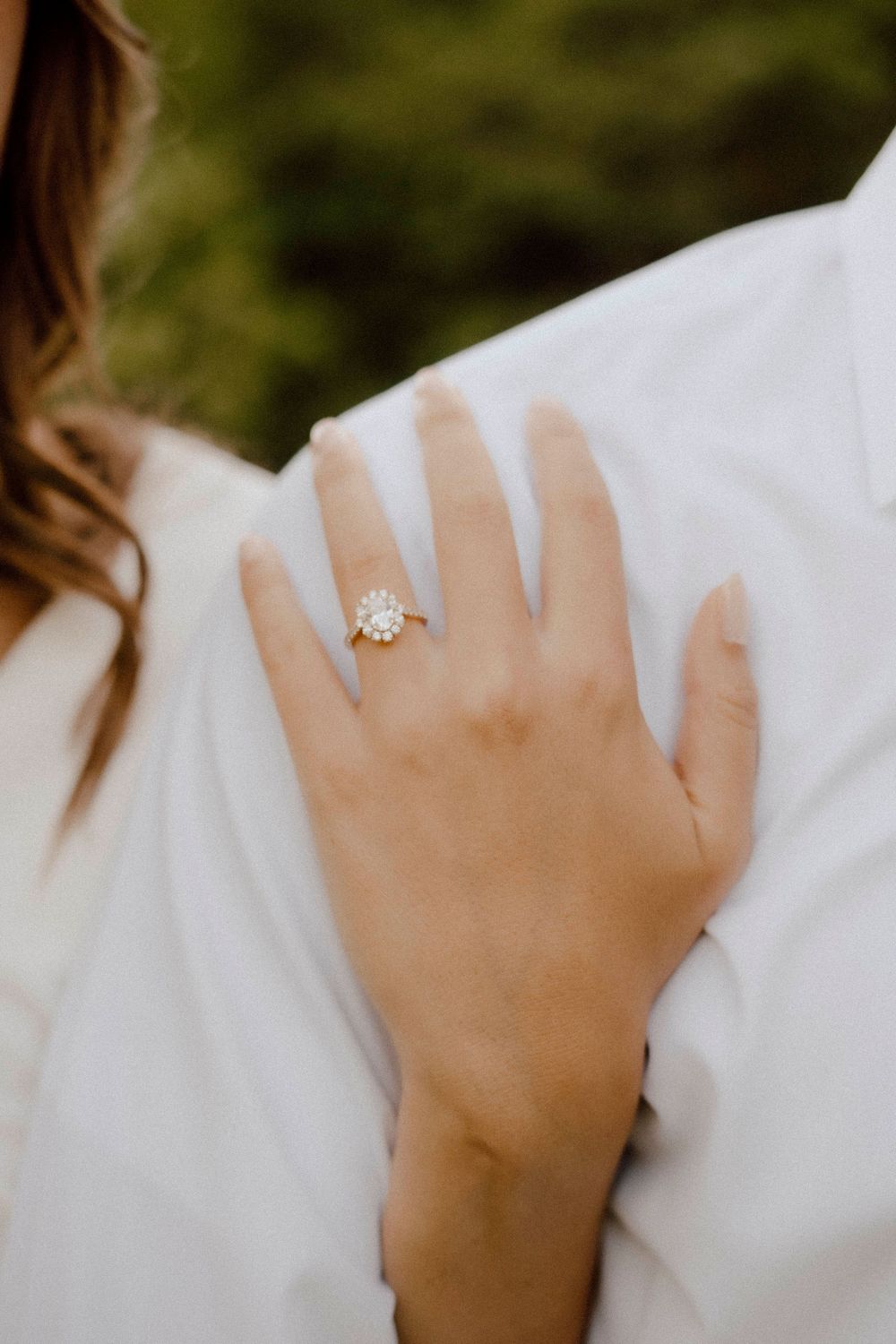 A delicate engagement ring sparkles against a white dress in natural light.