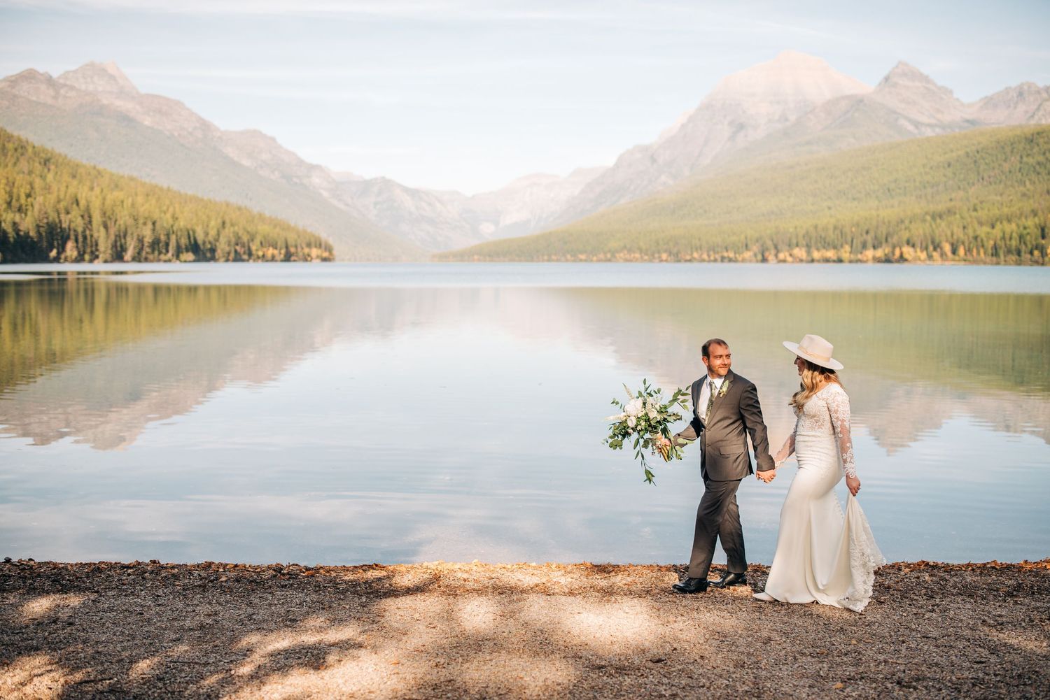 A romantic moment captured by a serene mountain lake with evergreen forests and peaks in the background.