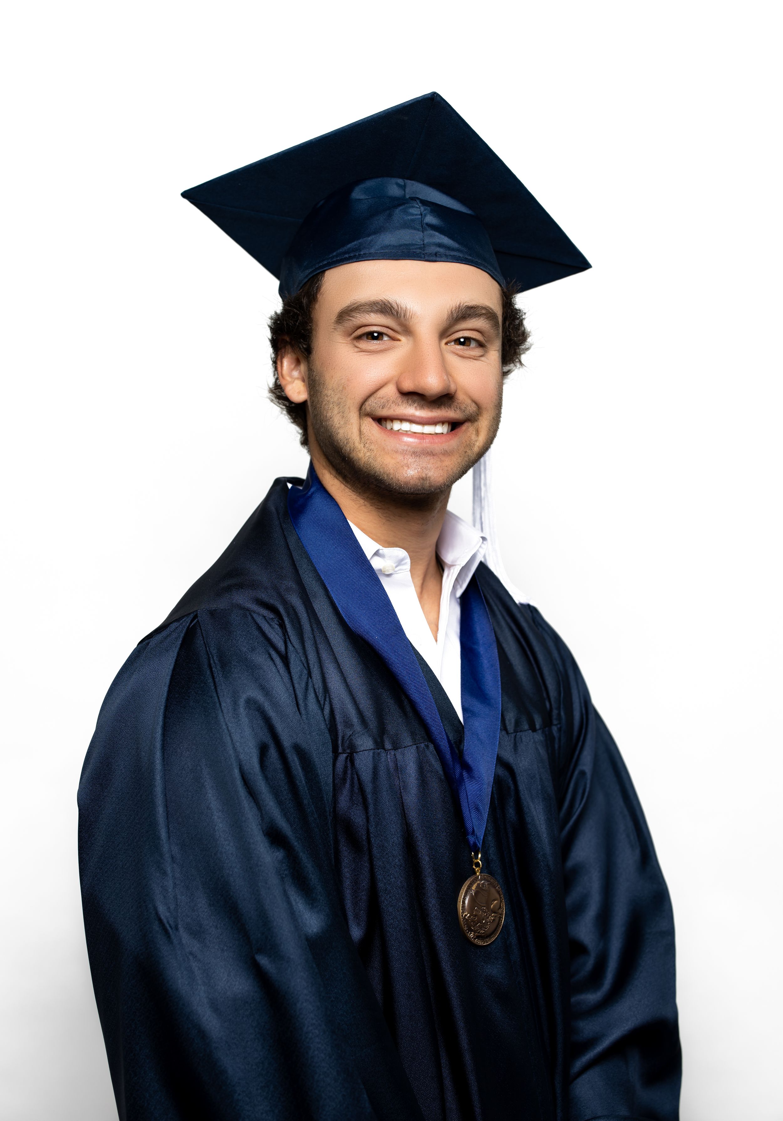 Graduate in navy blue cap and gown with medal smiling against white background.