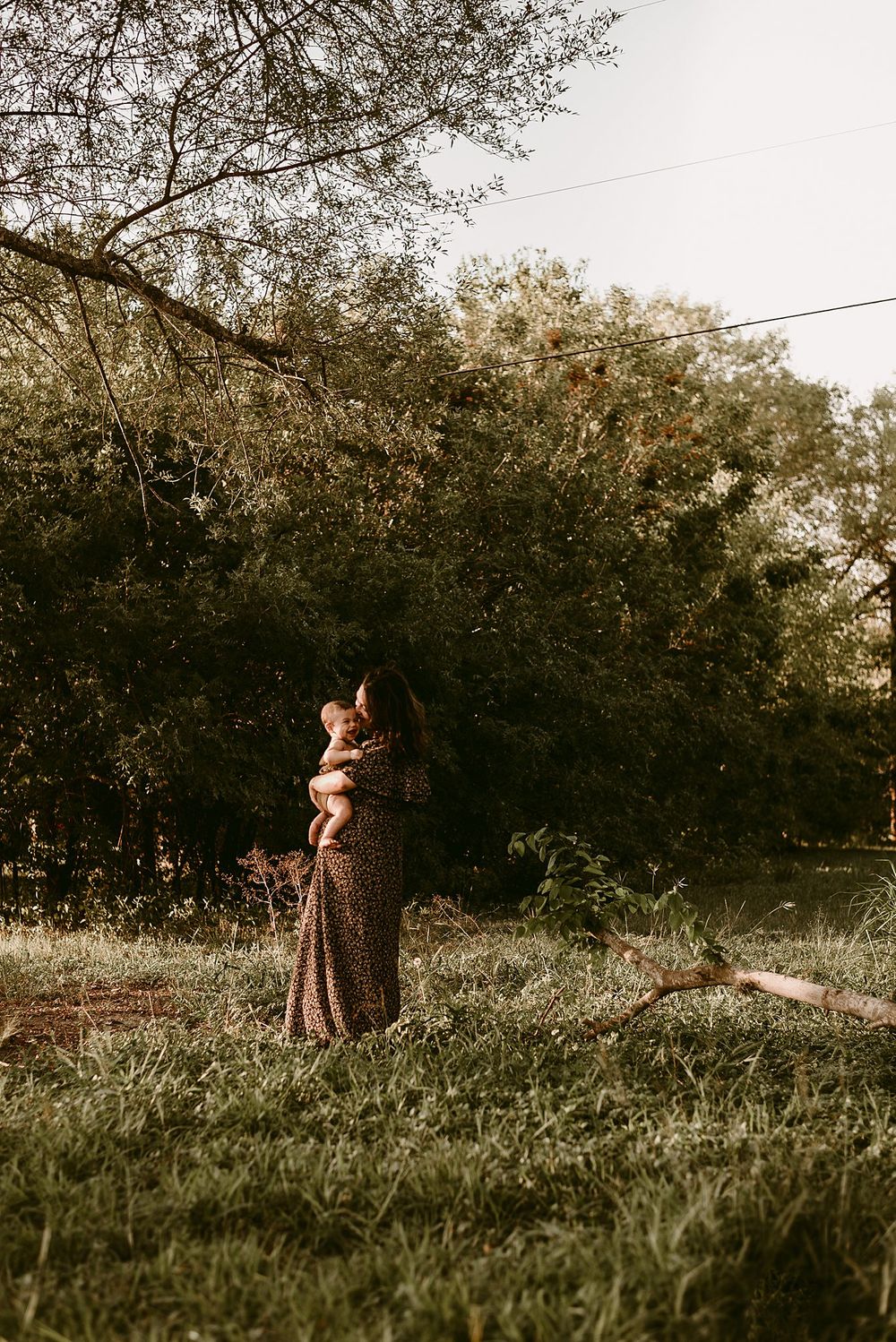 A dreamy outdoor portrait in a meadow with golden sunlight filtering through trees in the background.