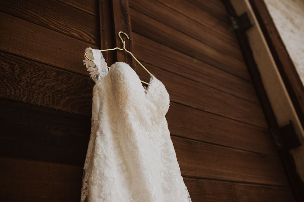 Elegant white wedding dresses hanging on wooden hangers against a rustic wall.