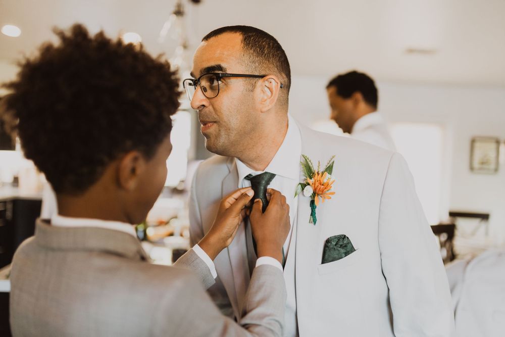 Wedding party members in light suits share laughs during pre-ceremony preparations.