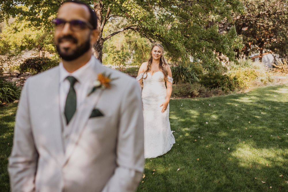 Wedding couple poses for first look photos in a sunny outdoor garden setting.