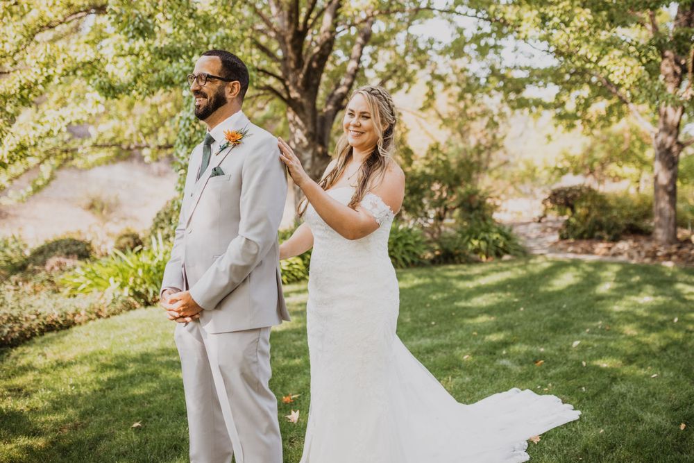 First look wedding photos captured in a sunlit garden with flowing white dress.