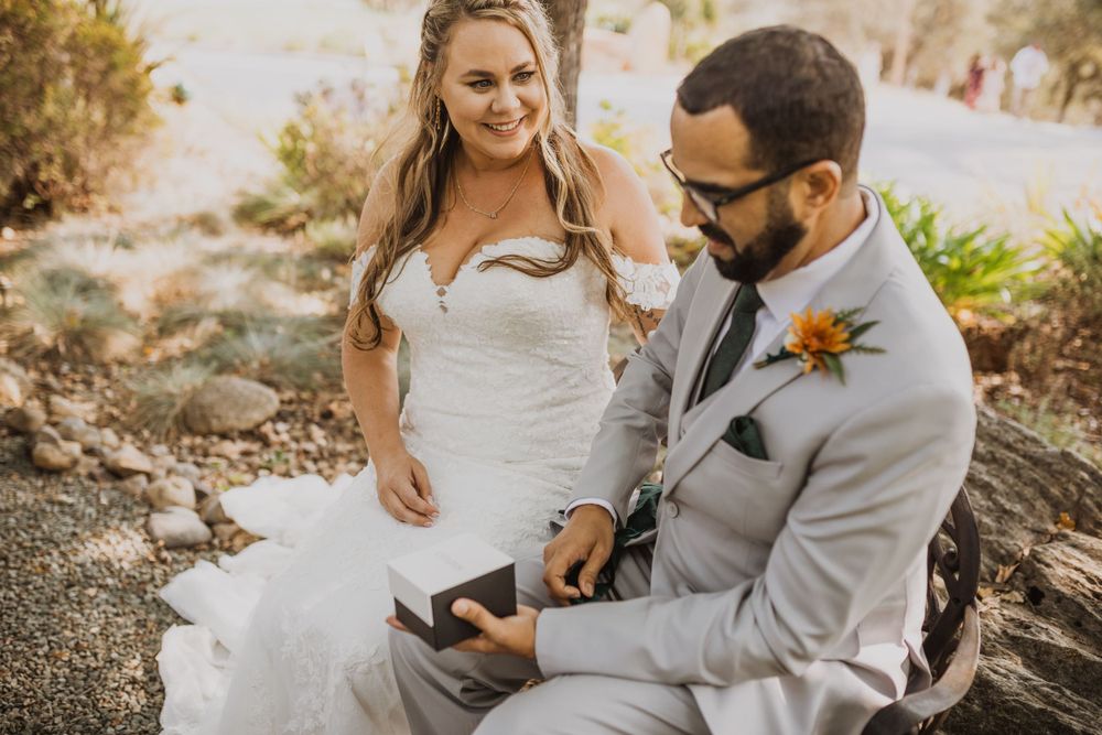 Newlyweds share laughter while sitting together on a rustic outdoor bench.