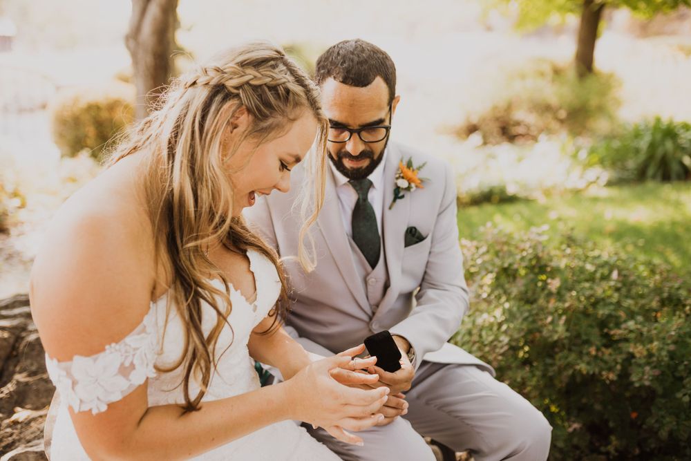 Wedding couple sits close together on outdoor bench during intimate ceremony.