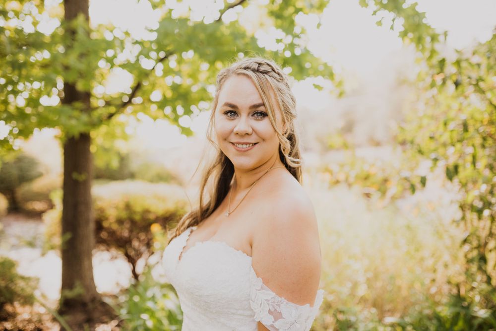 Bride smiles radiantly in white dress against natural outdoor backdrop.
