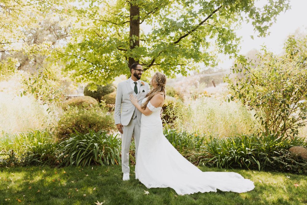 Wedding couple shares a tender moment in a lush garden setting with golden sunlight filtering through trees.
