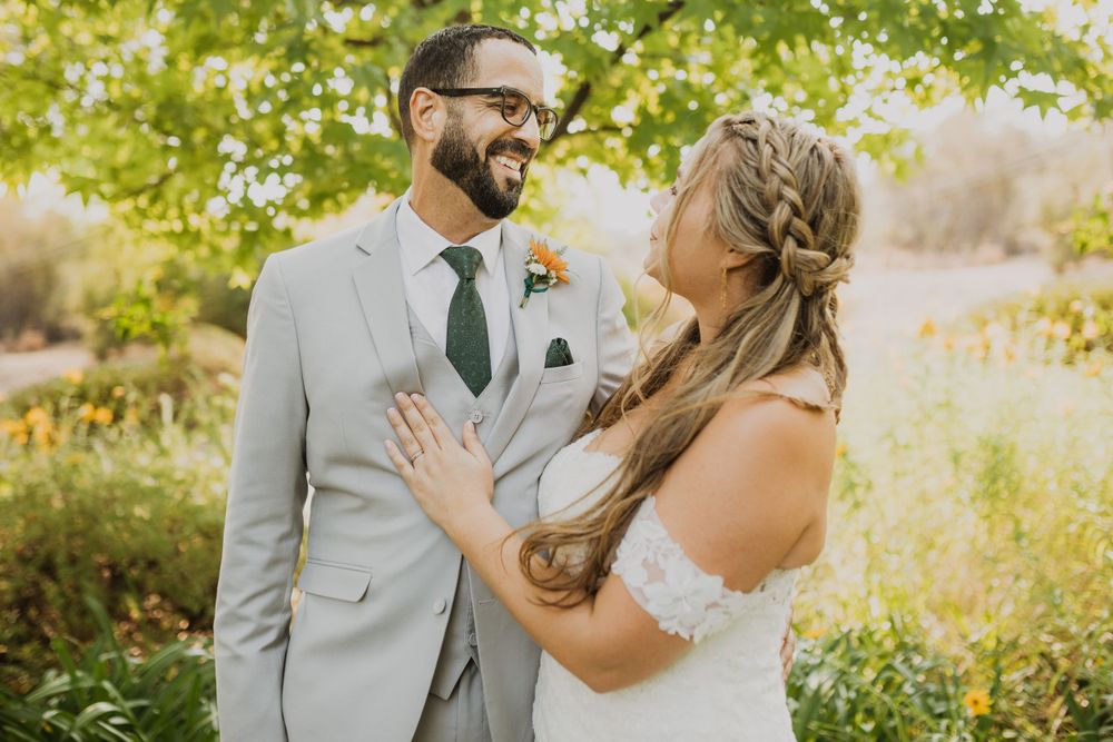 Bride and groom share joyful laughter during their outdoor wedding photoshoot surrounded by greenery.