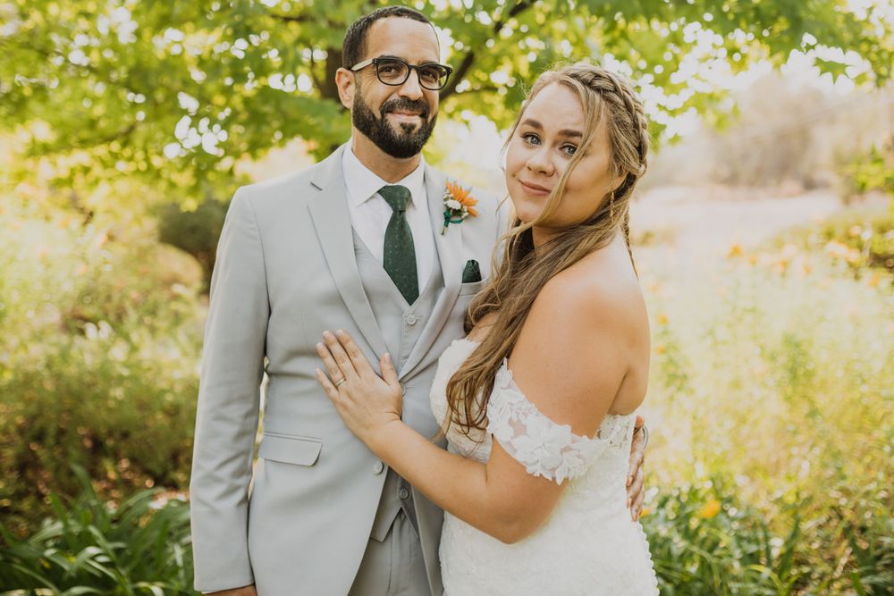 Newlyweds embrace in a sunlit garden wearing elegant wedding attire.