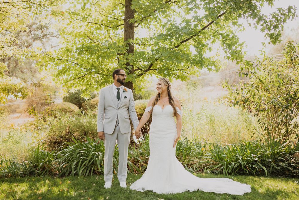 Elegant wedding couple poses in a garden with natural sunlight streaming through trees.