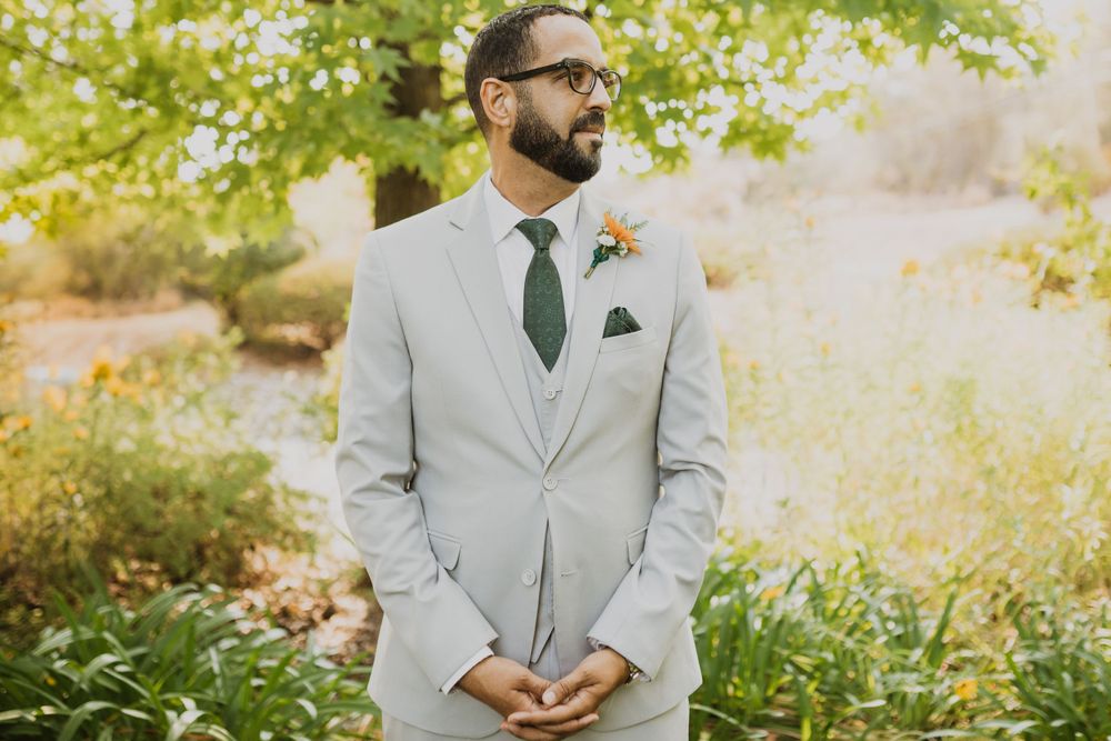 Groom in light grey suit stands in a serene garden setting during wedding photography.