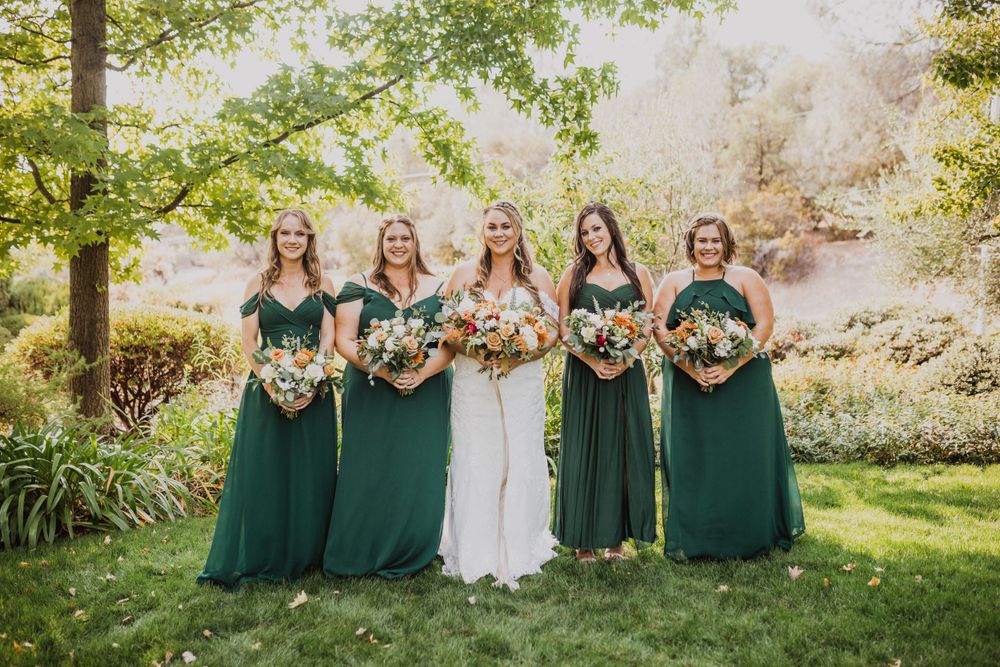 Bridal party in emerald green dresses poses together outdoors for wedding photos.