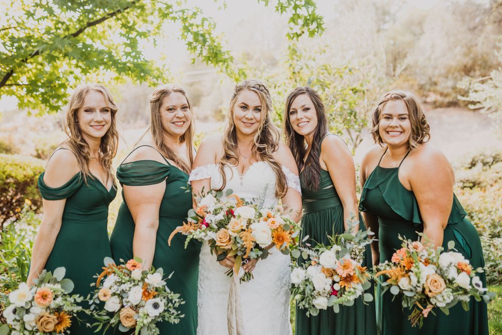 Wedding party with bridesmaids in dark green dresses holds vibrant floral bouquets.