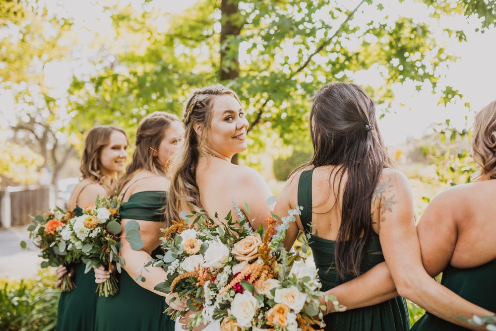 Bridesmaids in emerald dresses share candid moment during outdoor wedding photography.