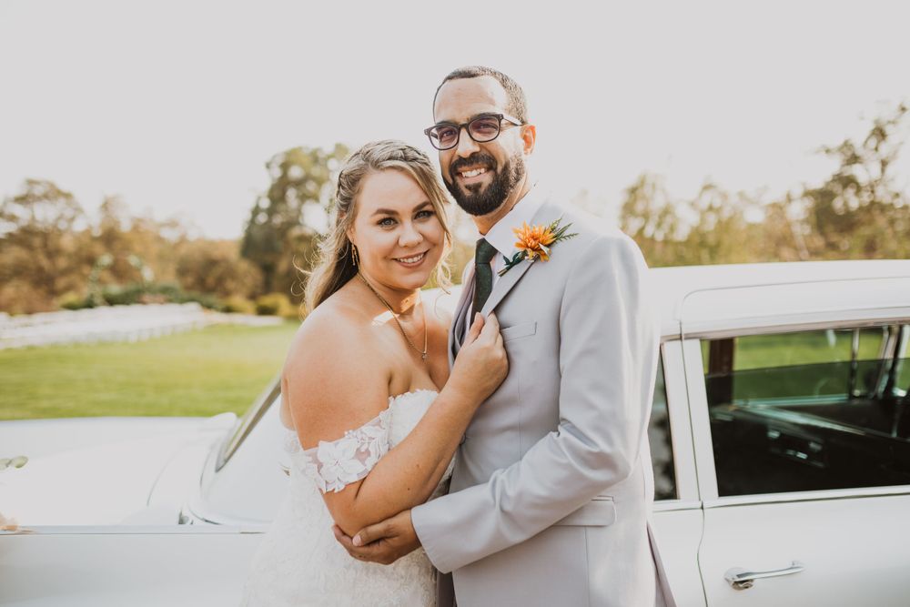 Wedding couple poses near vintage car during outdoor photo session.
