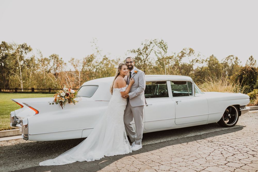 Elegant couple posing beside a vintage white limousine at their outdoor wedding.