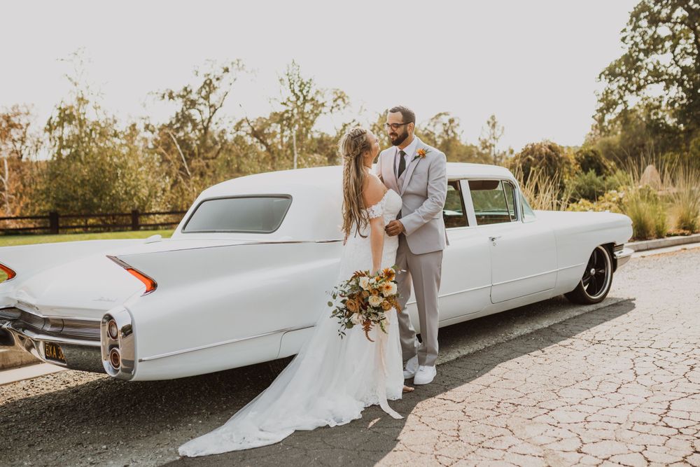 Wedding couple sharing intimate moment next to classic white limousine on stone pathway.