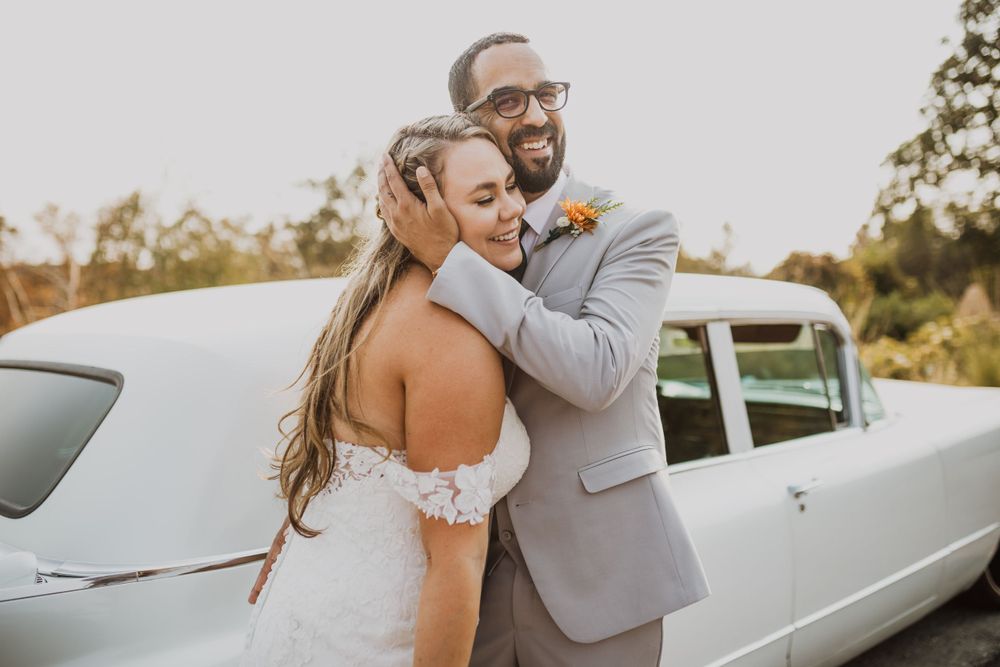 Romantic wedding portraits taken beside vintage white limousine during golden hour.