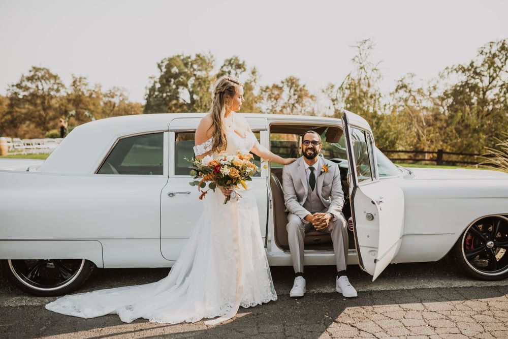 Wedding couple embracing by classic white limousine against natural outdoor backdrop.