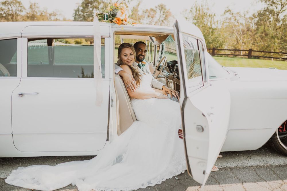 Classic white vintage car parked outdoors with wedding couple by the door at sunset.