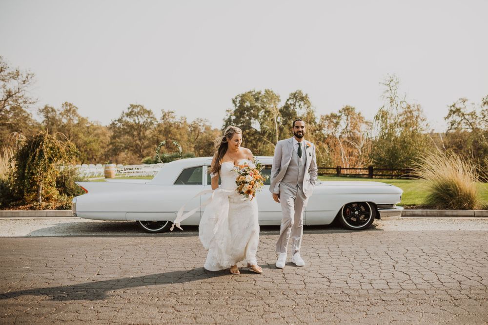 Elegant wedding party photo session with vintage white car in natural outdoor setting.