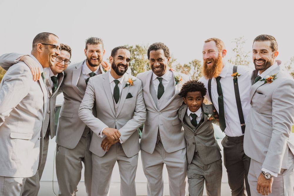 Groomsmen in light gray suits pose together outdoors for wedding photos.