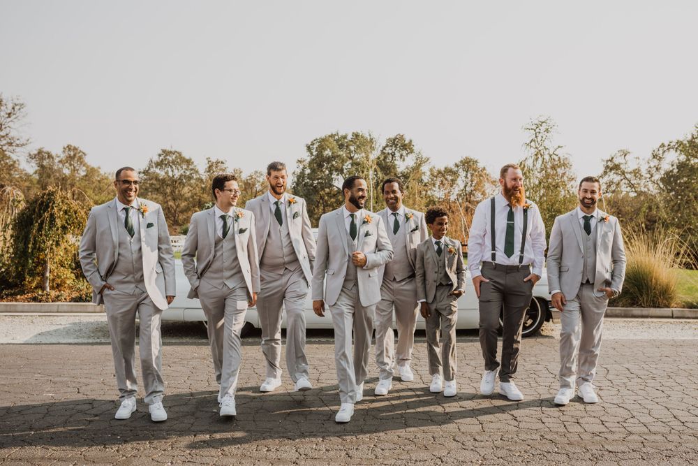 Groomsmen walking in formation wearing matching light gray suits and navy ties.