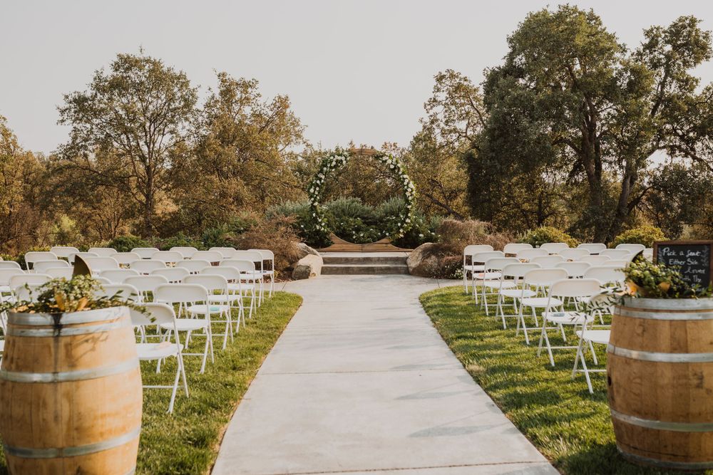 Wedding venue with rustic wine barrels and white chairs arranged along concrete pathway.