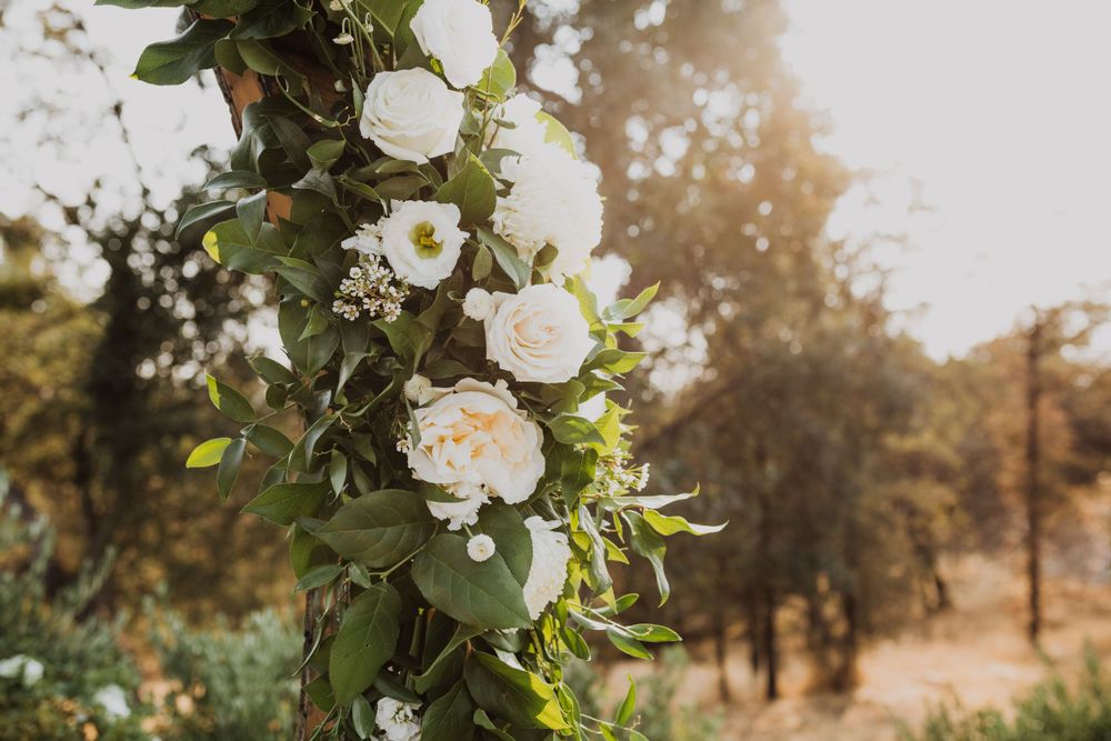White roses and greenery arrangements decorating outdoor wedding venue.